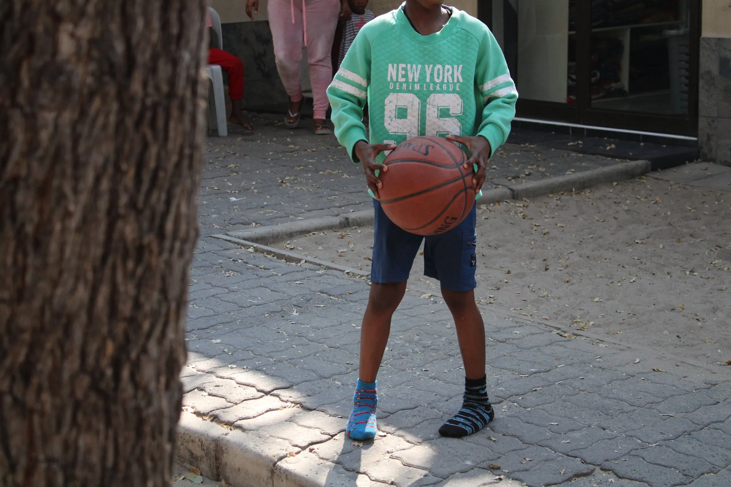 A child holding a basketball in the Lorato House playground, seen from behind