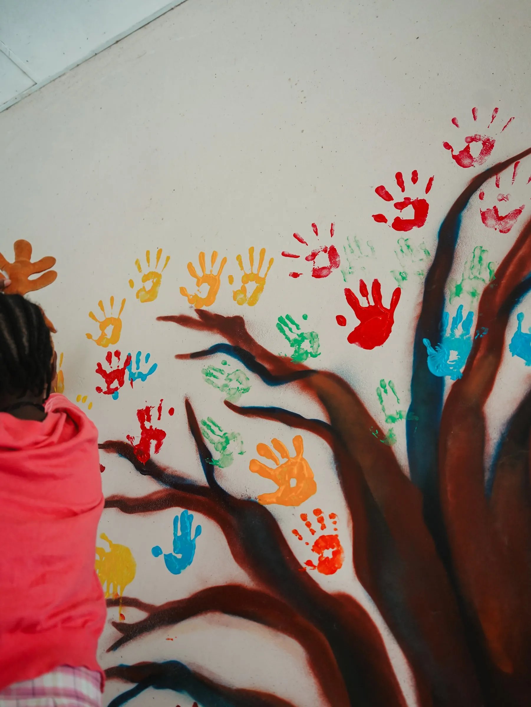 A child adding a painted handprint to the Lorato House handprint tree mural