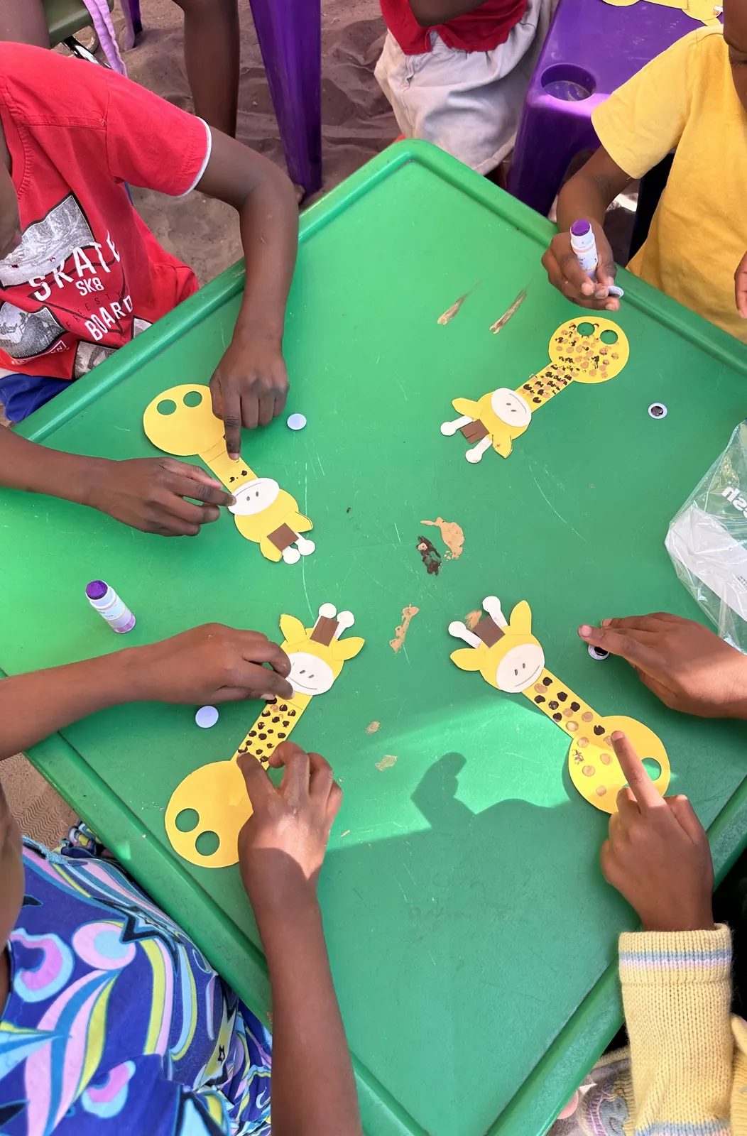 Children's hands making paper giraffe crafts at a table
