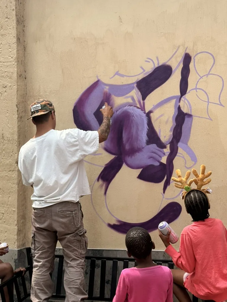 An artist painting a mural while children watch from behind