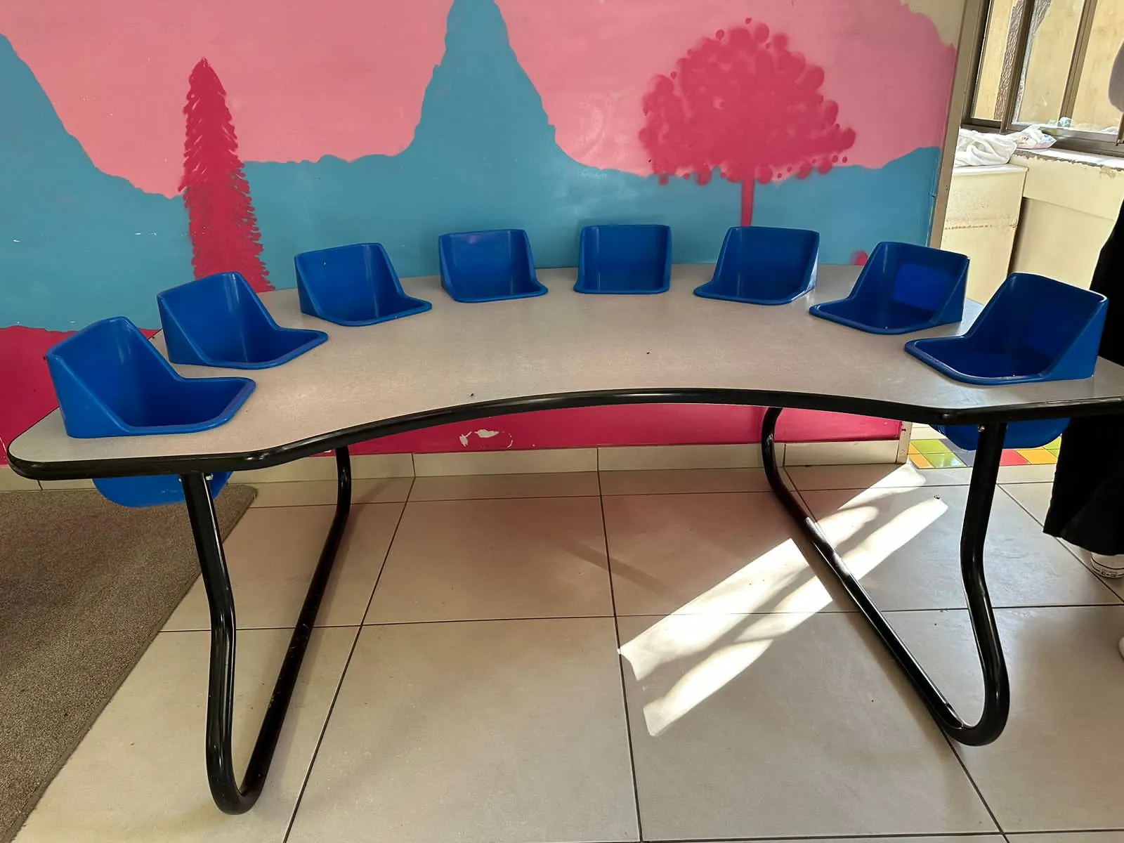 A children's table with blue seats in front of a painted wall