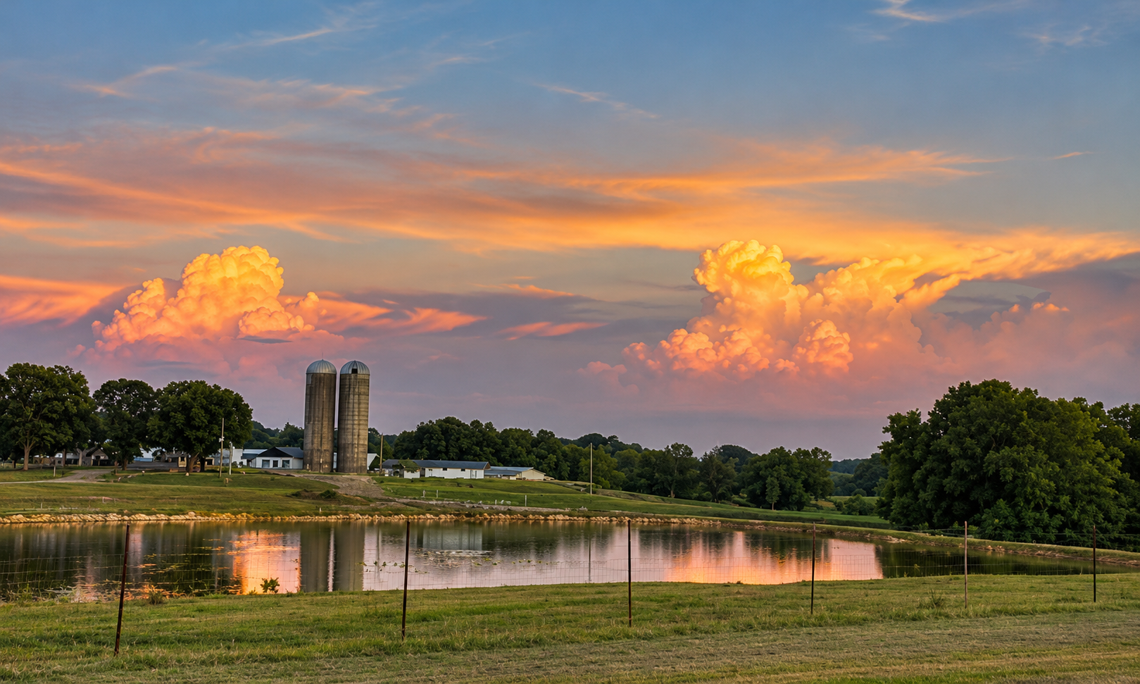 Orange and pink sunset clouds above the farm pond and pasture.