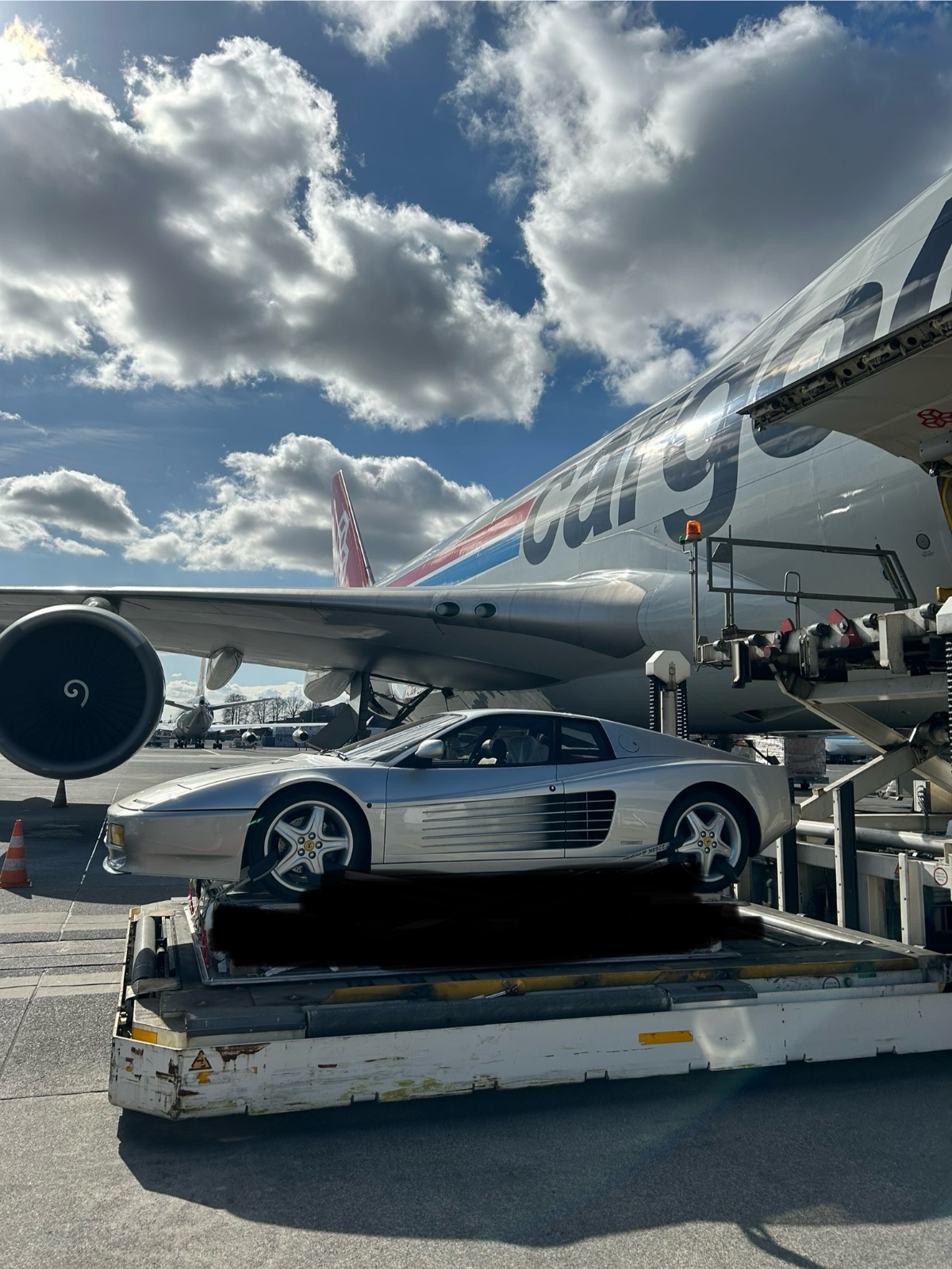 Ferrari Testarossa sanglée sur palette avion devant un Boeing 747 Cargolux