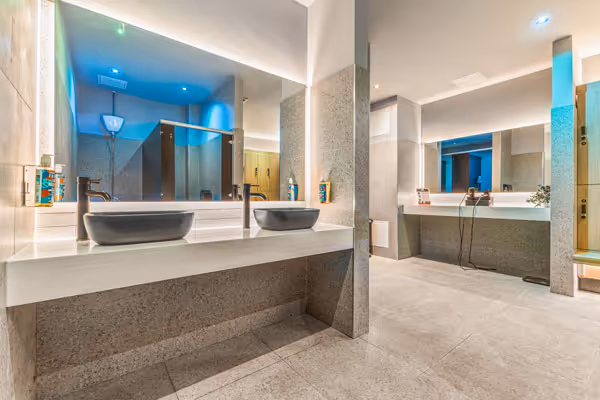 Modern bathroom vanity area with two round stools, a large mirror, and hairdryers on the countertop.