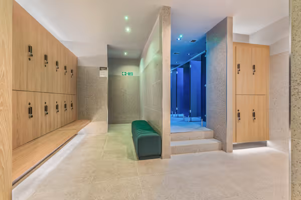 Modern locker room with wooden lockers, a green bench, and blue-lit shower stalls.
