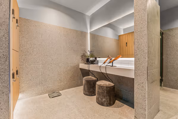 Modern dressing room with two round stools, wall mirror, and hairdryers on white countertop.