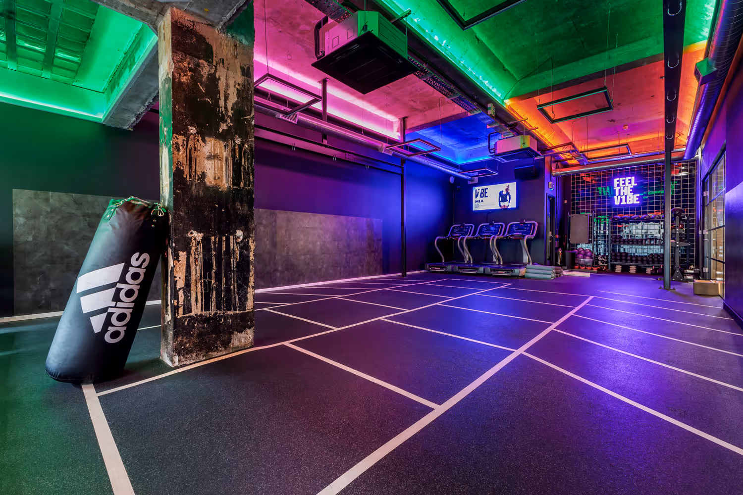 Modern gym room with colorful neon lights, treadmills, Adidas punching bag, and fitness equipment.