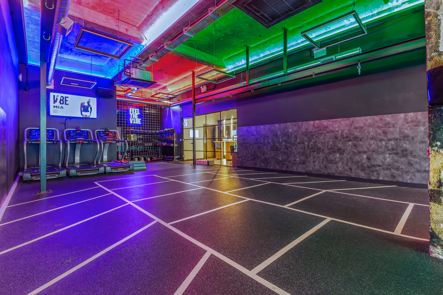 Modern gym area with colorful ceiling lights, treadmills, and open workout space marked with white lines.