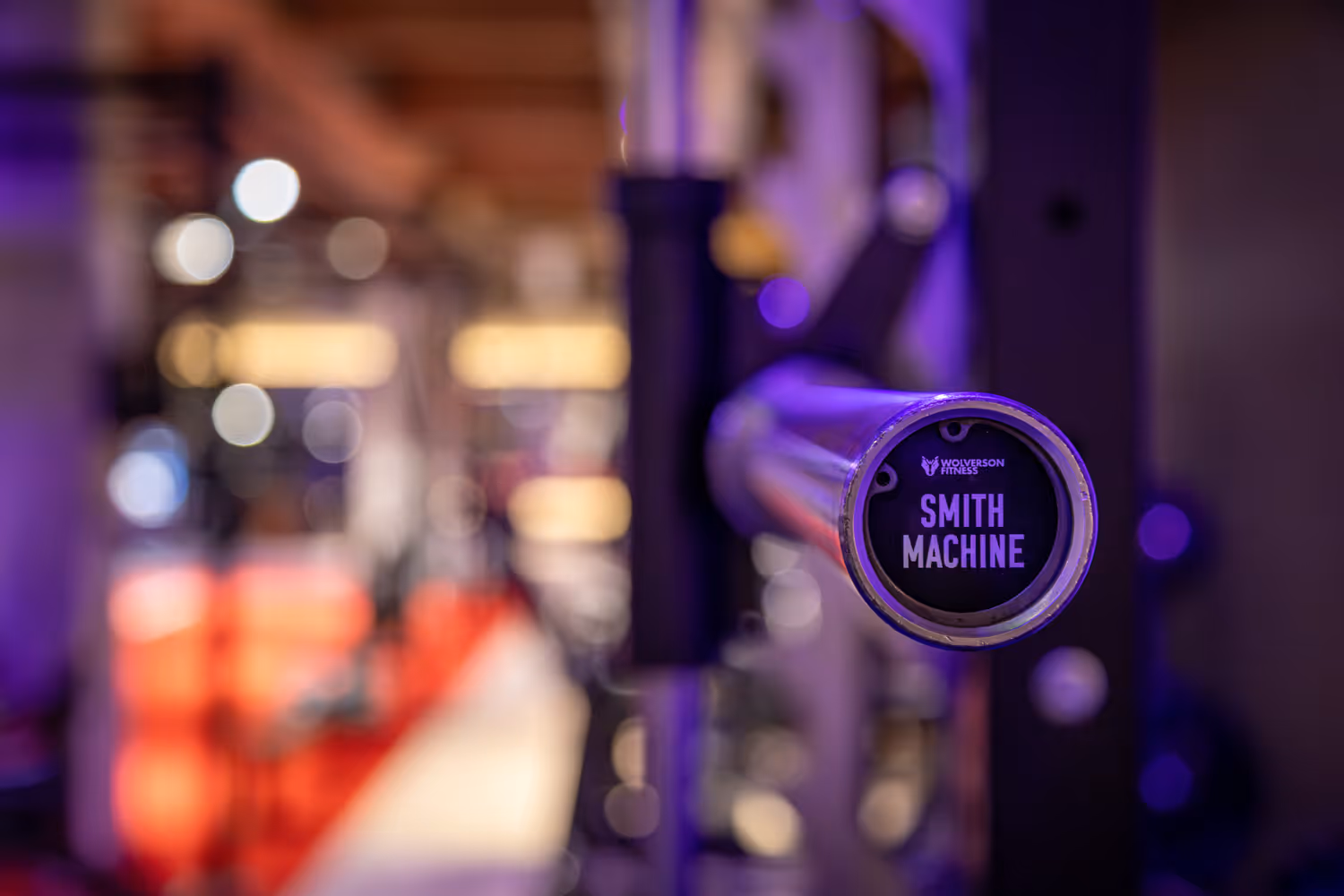 Close-up of a Smith machine barbell in a gym with blurred background lights.