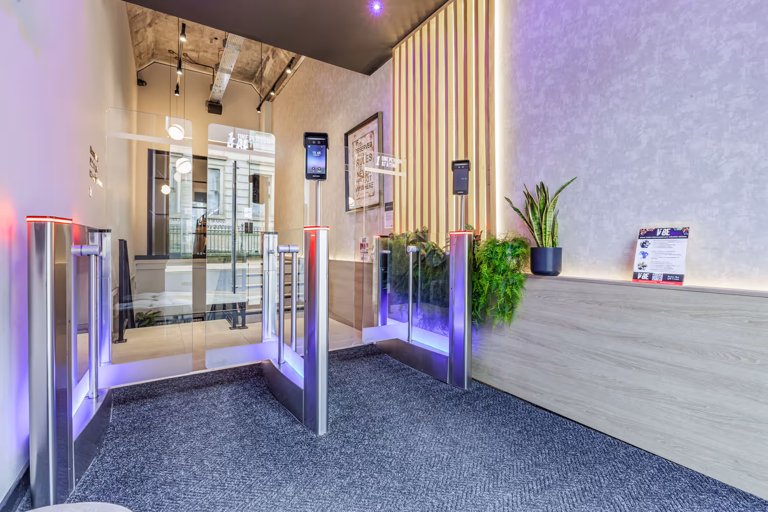 Modern office entrance with biometric turnstiles, glass doors, and potted plants on a wood counter.