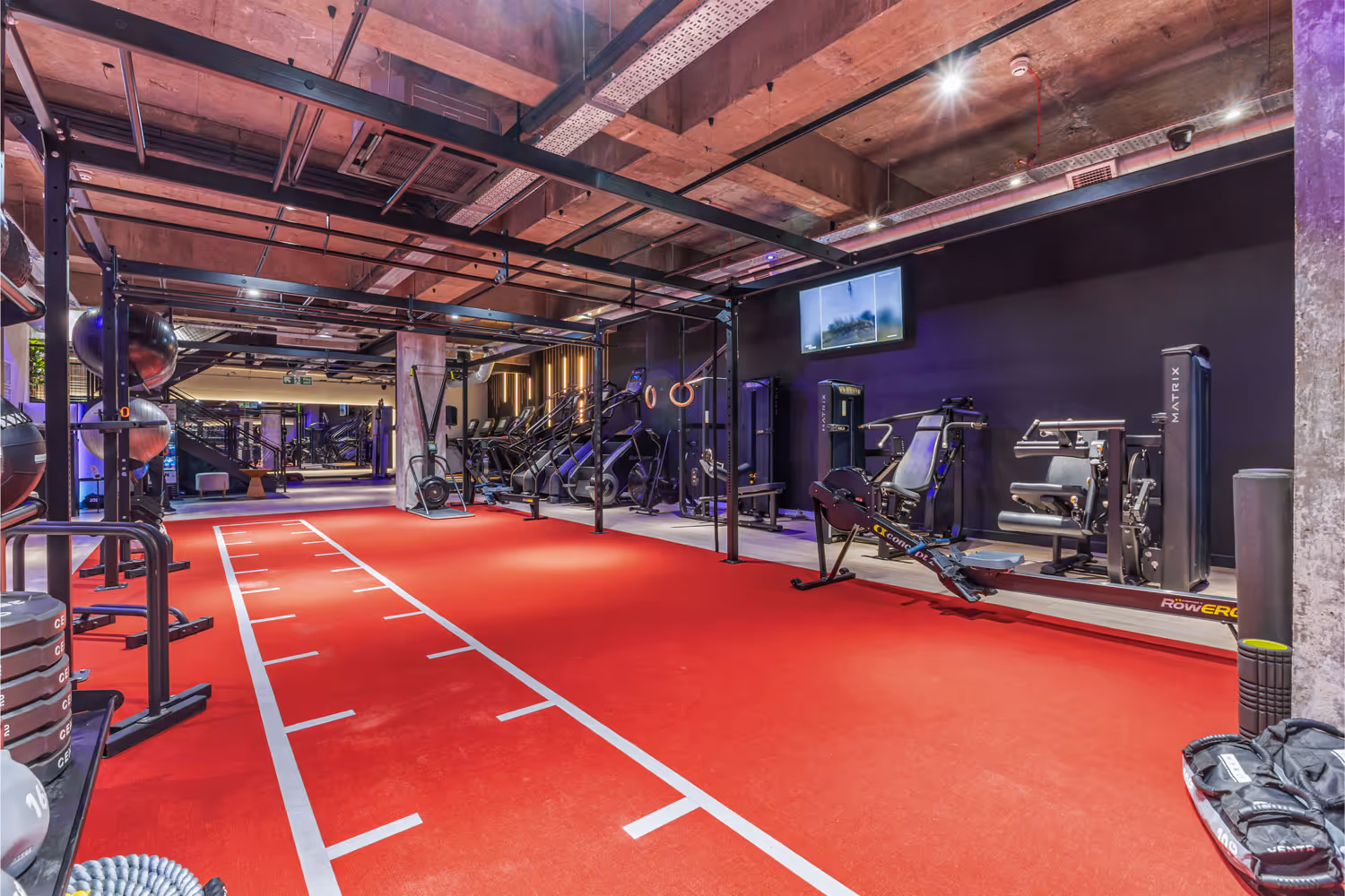 Modern gym with red floor, exercise balls, weights, and metal workout frame with rings.