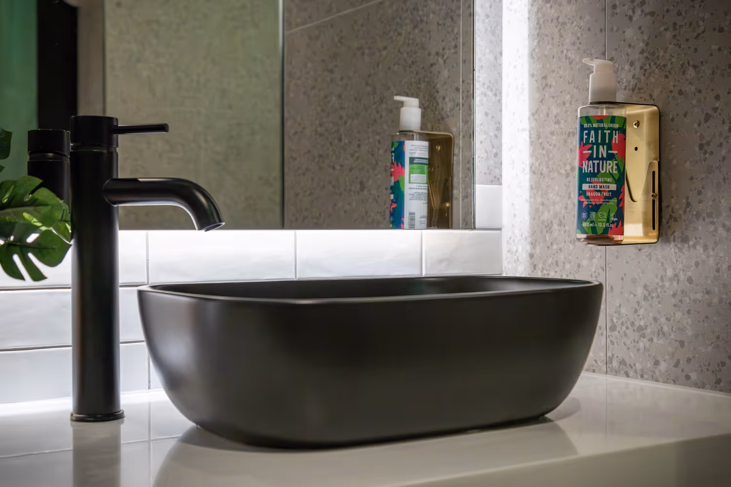 Modern black faucet and rectangular black sink with a colorful Faith in Nature soap dispenser on wall.