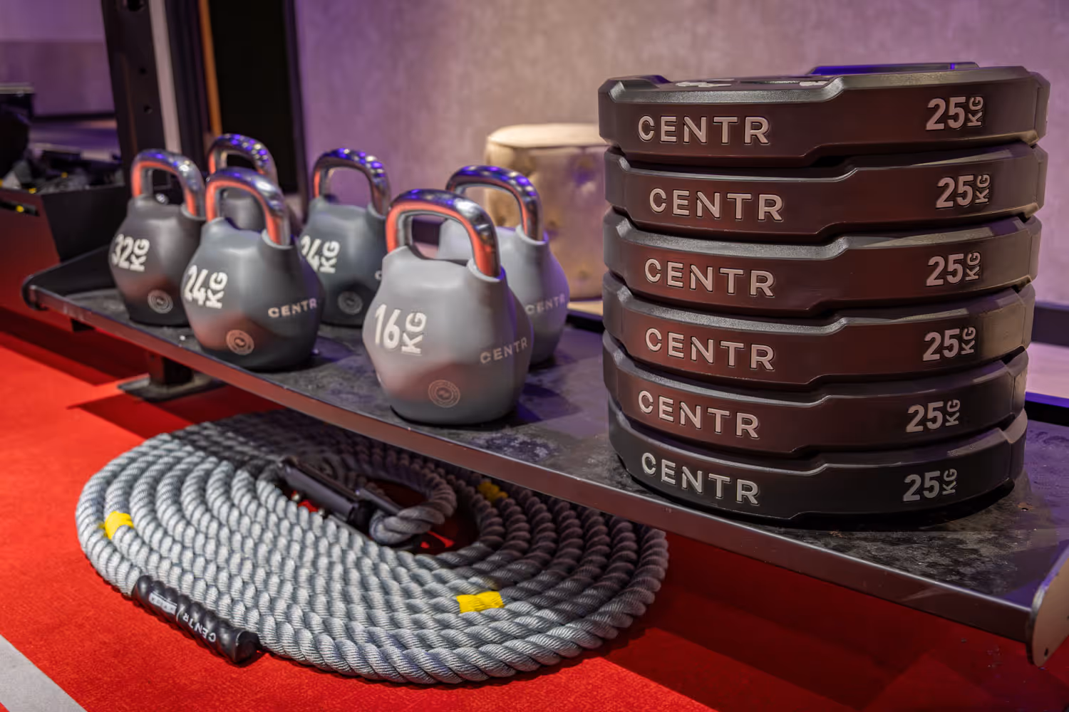 Kettlebells and stacked weight plates labeled CENTR on a gym shelf with battle ropes below.