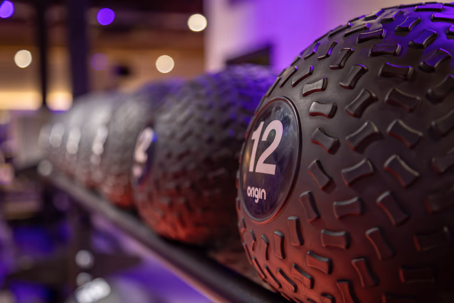 Close-up of a textured exercise medicine ball labeled 12 on a gym rack with blurred balls behind.