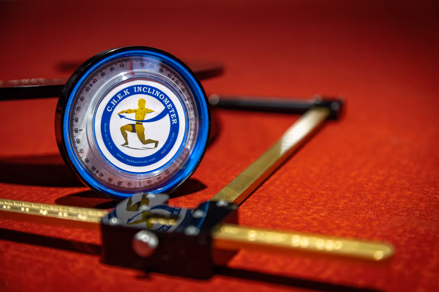 Close-up of a C.H.E.K inclinometer on a red surface with gold measurement arms extended.