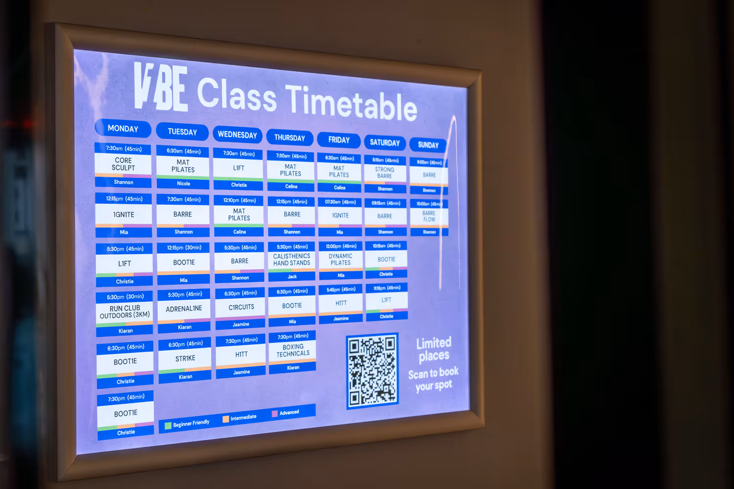 Digital VIBE Class Timetable display showing weekly fitness classes and times with a QR code to book.