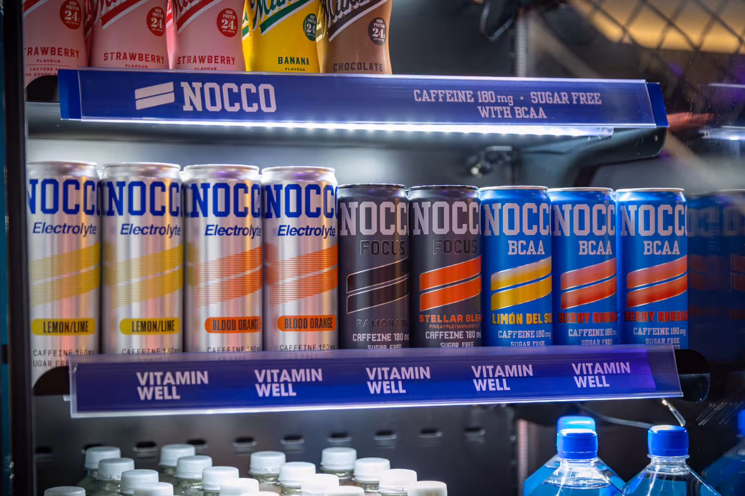 Shelf of NOCCO energy drink cans in flavors lemon lime, blood orange, focus, and BCAA in a refrigerator.