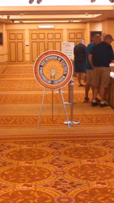 Sign for International Brotherhood of Electrical Workers in a carpeted conference room with people at a table.