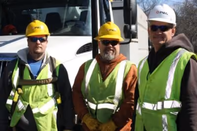 Three construction workers in high-visibility vests and hard hats standing outside near a truck.