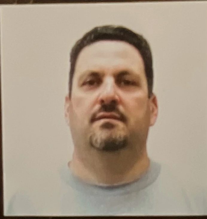 Headshot of a man with short dark hair, goatee, and a neutral expression wearing a gray shirt.