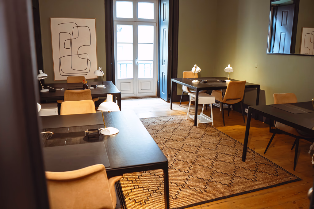 Modern office with black desks, tan chairs, white lamps, patterned rug, and large window door.