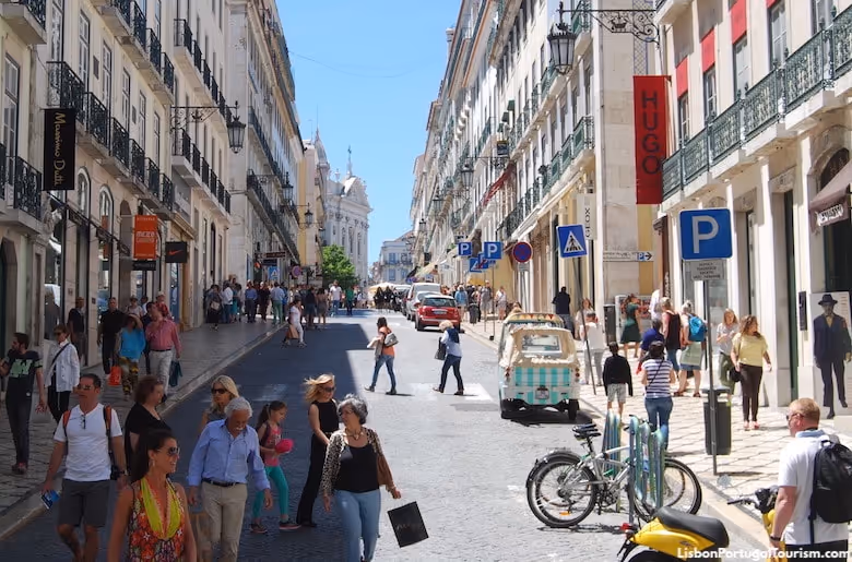 Busy street in Chiado Lisbon with pedestrians, parked bikes, shops, and historic buildings under blue sky.