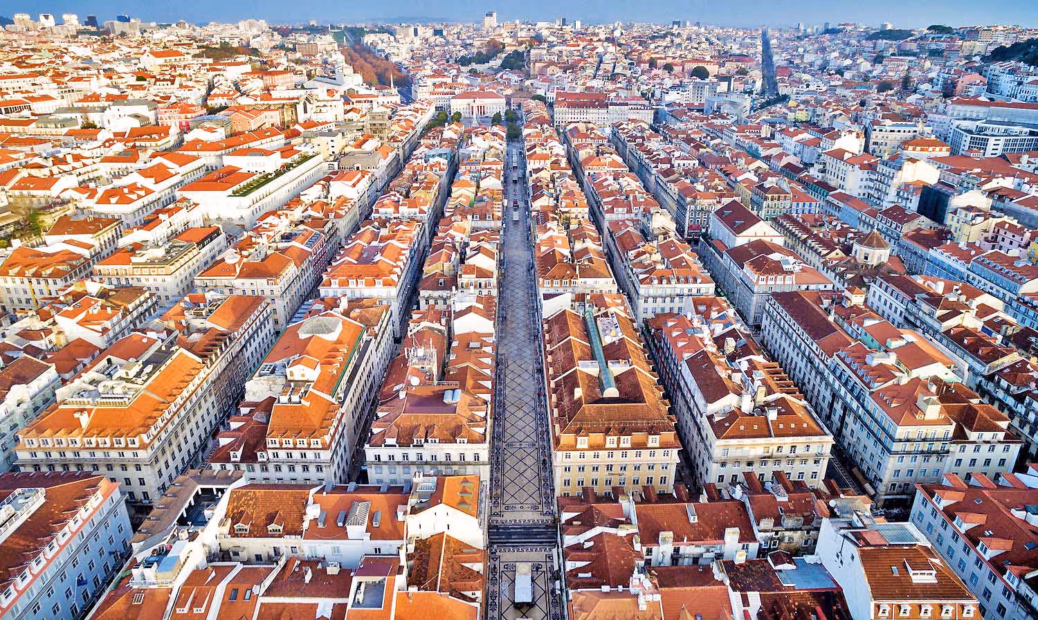 Aerial view of a grid-like cityscape with orange rooftops and a long patterned pedestrian street.