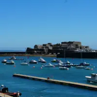 Small boats moored in St Peter Port harbour with Castle Cornet in the background under a clear blue sky.