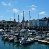 Sailboats docked in St Peter Port with high-street buildings and blue sky in the background.