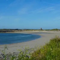 Vazon beach with calm blue water under clear sky and vegetation on the shore.