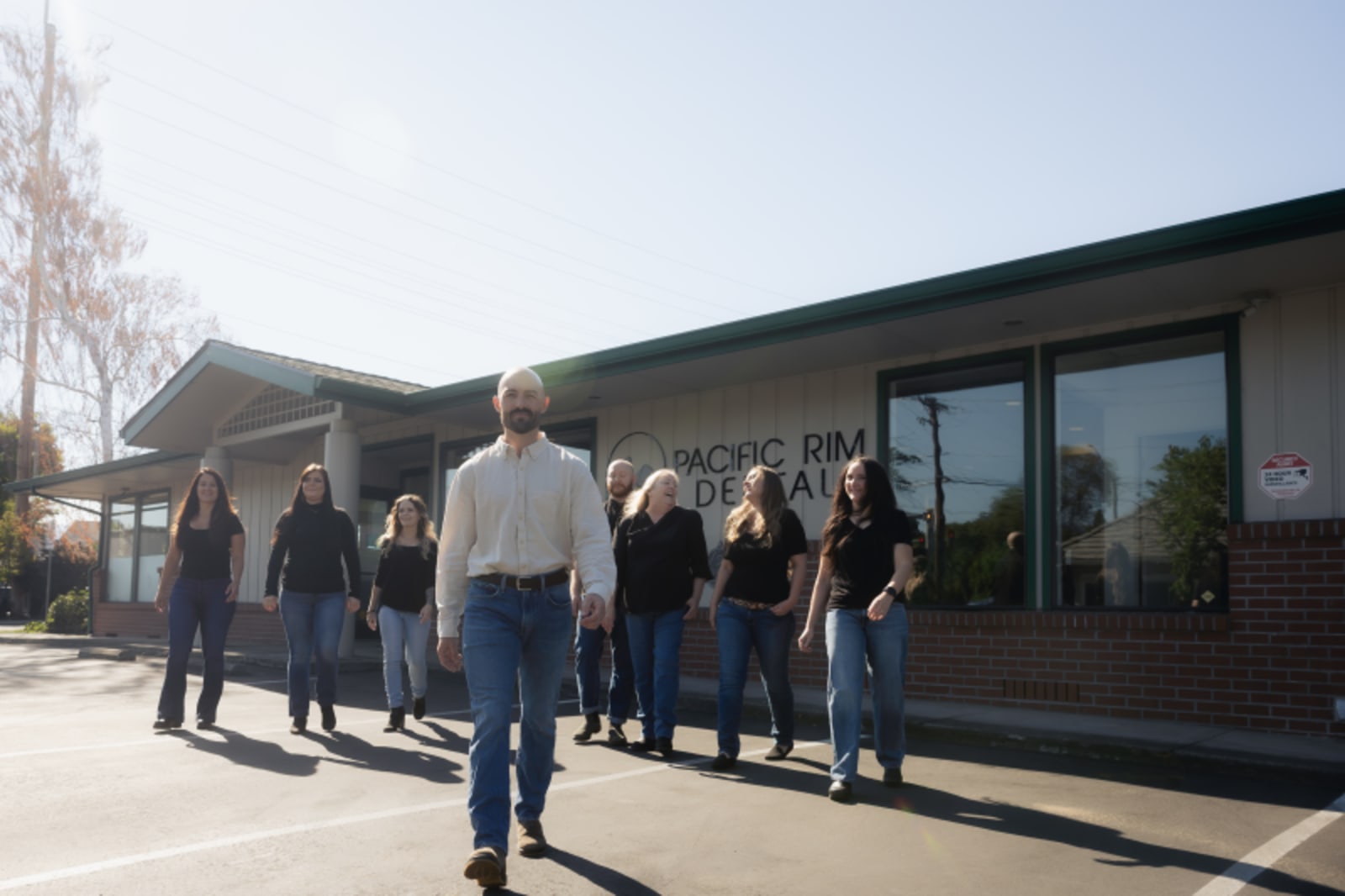 Group of people standing outside a modern dental office building on a sunny day.