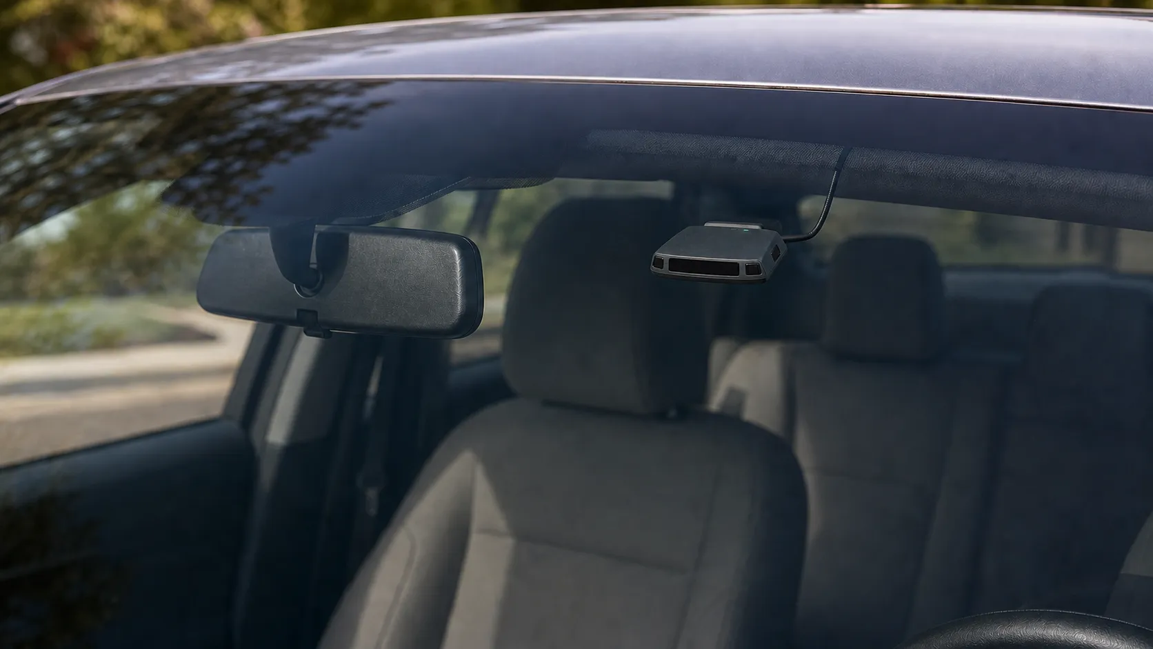 View through a vehicle windshield showing the BanditKin Sentinel mounted high near the rear-view mirror with its receiver face aimed outward and its USB-C cable entering the headliner. Render.