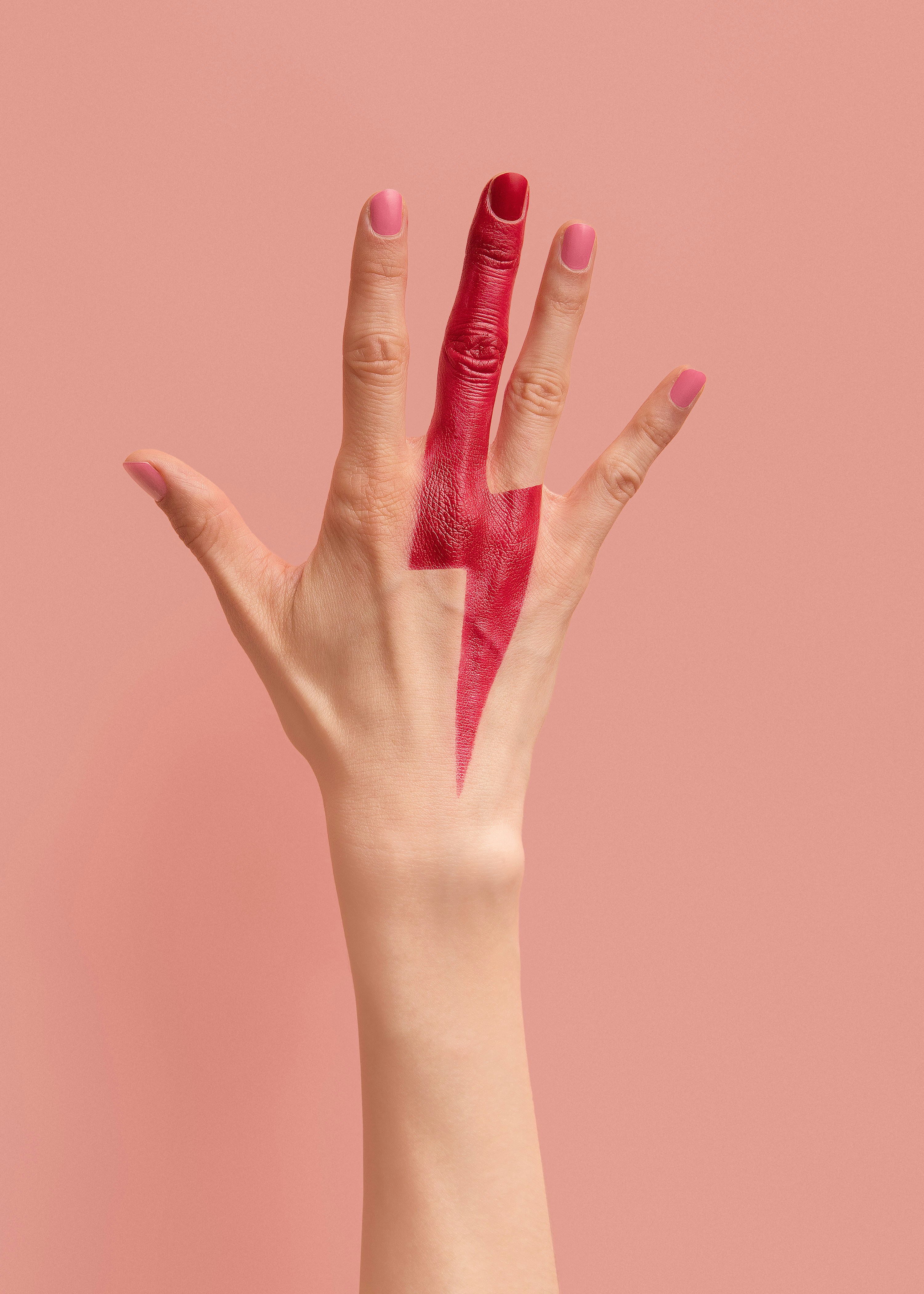 Main levée avec un éclair rouge peint sur le majeur contre un fond rose.