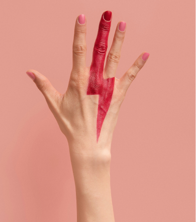 Main féminine avec peinture rouge en forme d'éclair sur l'annulaire contre un fond rose.
