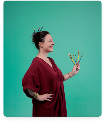 Femme souriante de profil en robe rouge tenant des pinceaux sur fond turquoise.