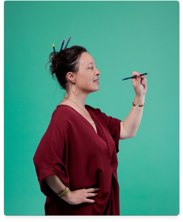 Femme souriante en robe rouge tenant des pinceaux avec d'autres dans ses cheveux sur fond vert.