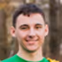 Smiling young man wearing a green sports jersey outdoors.