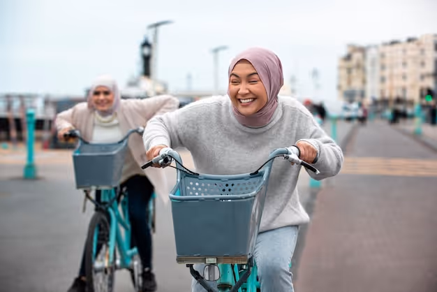 Two women wearing hijabs smiling and riding bicycles on a city street.