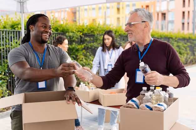 Two volunteers exchanging a water bottle while packing boxes of food and supplies outdoors.