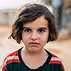 Portrait of a child with short dark hair and serious expression wearing a dark shirt with red and white stripes on the shoulders.