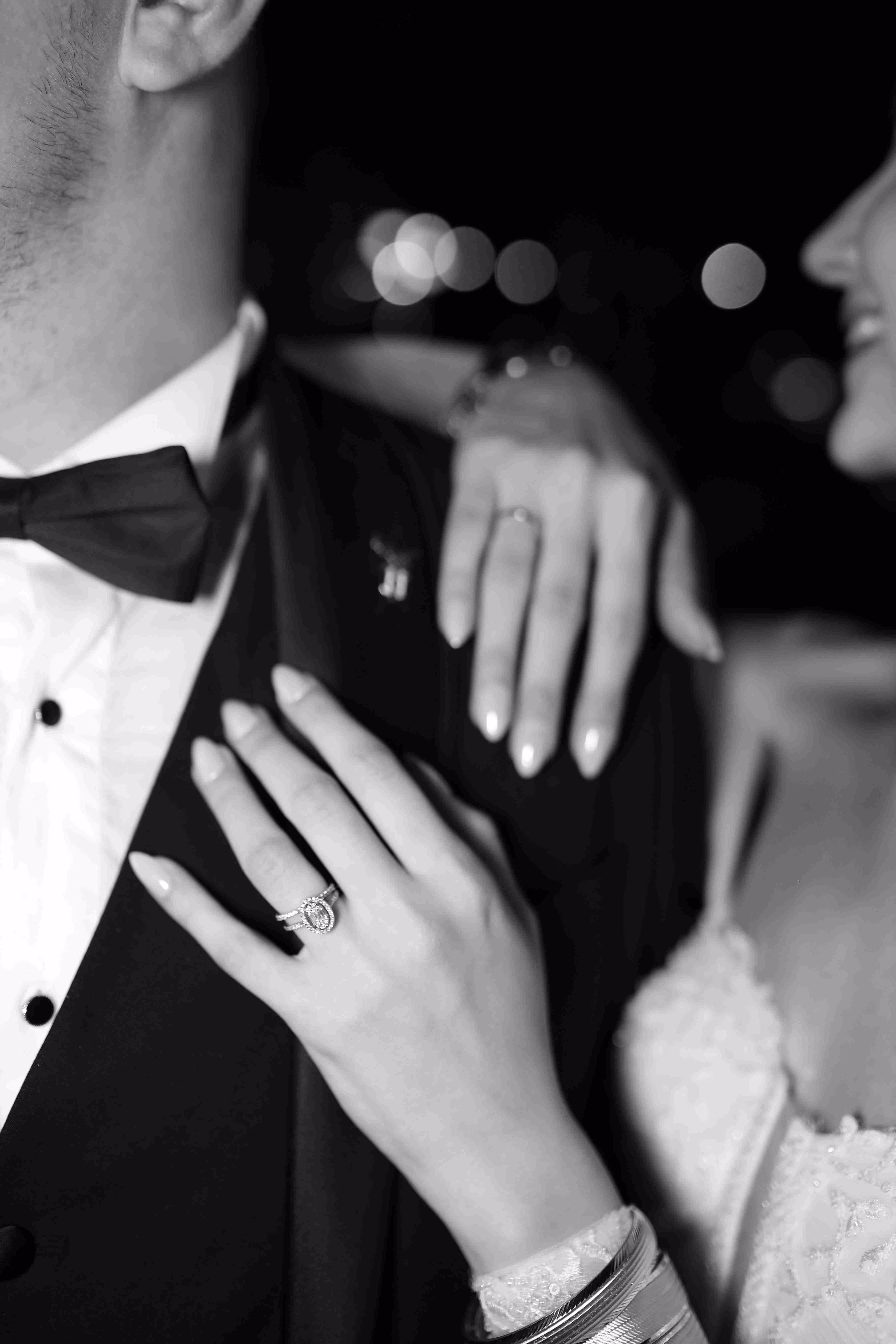 Bride's hands with wedding rings resting on groom's suit jacket and shoulder.