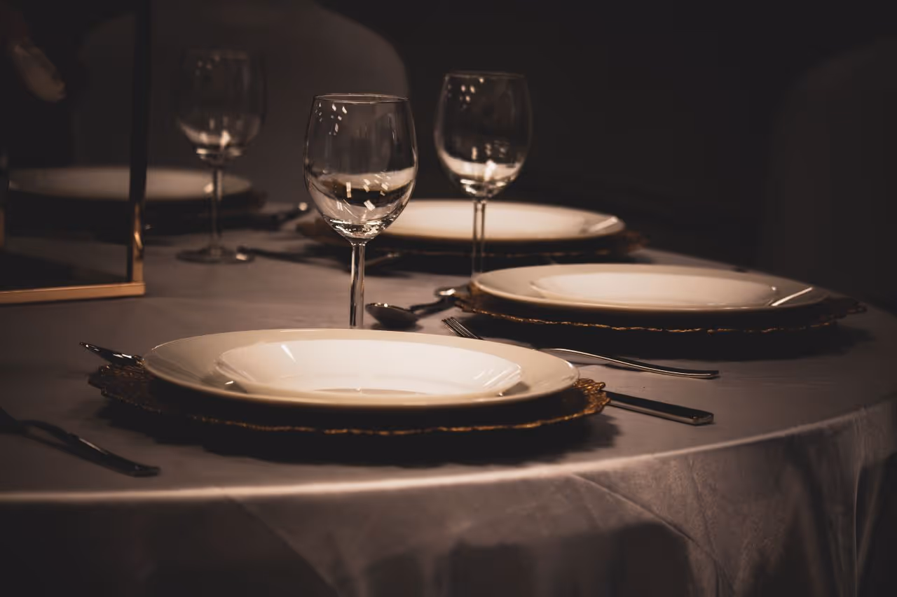 Elegant dining table with white plates, silver cutlery, and empty wine glasses on a white tablecloth.