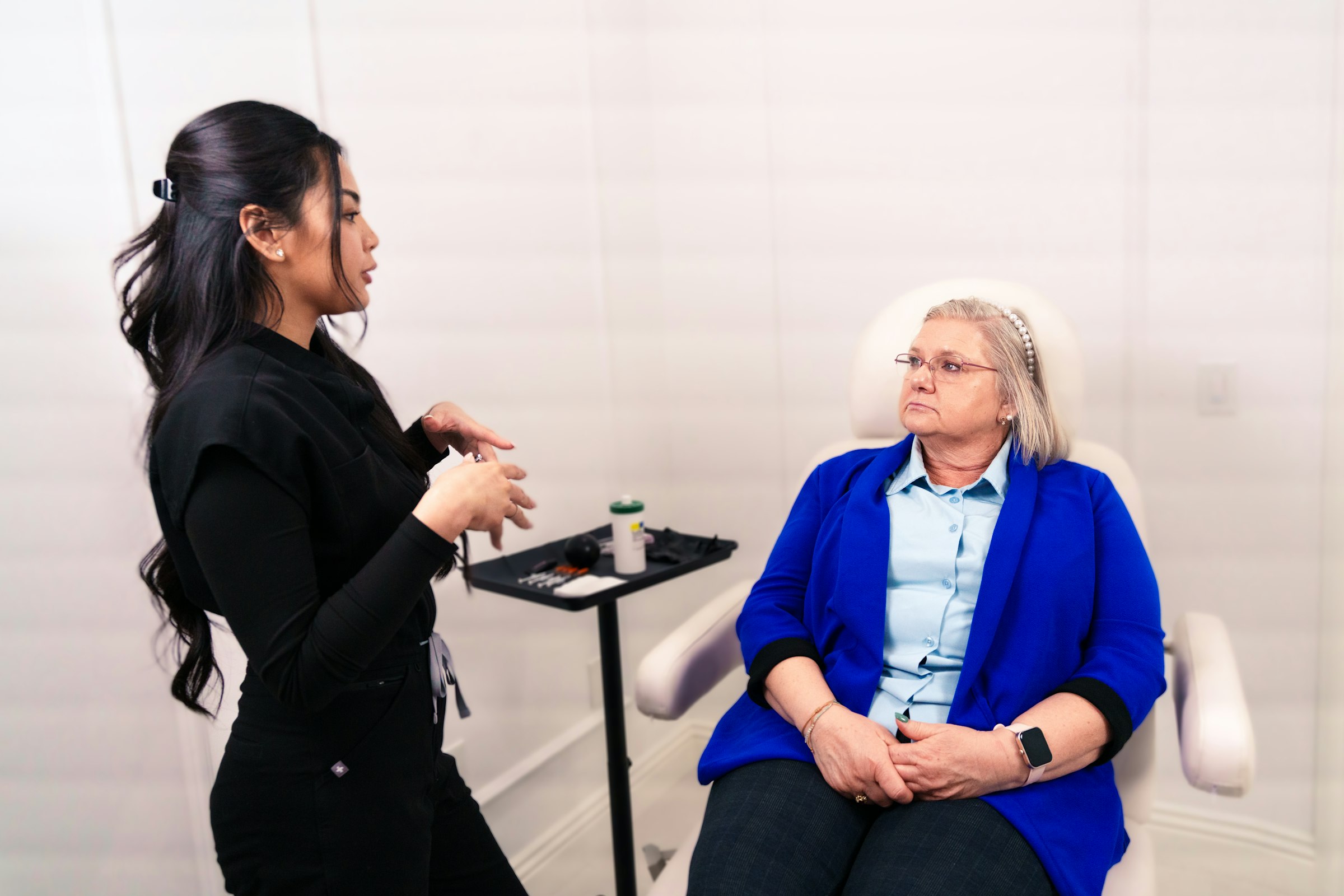 An aesthetics practitioner in consultation with a seated client in a treatment room