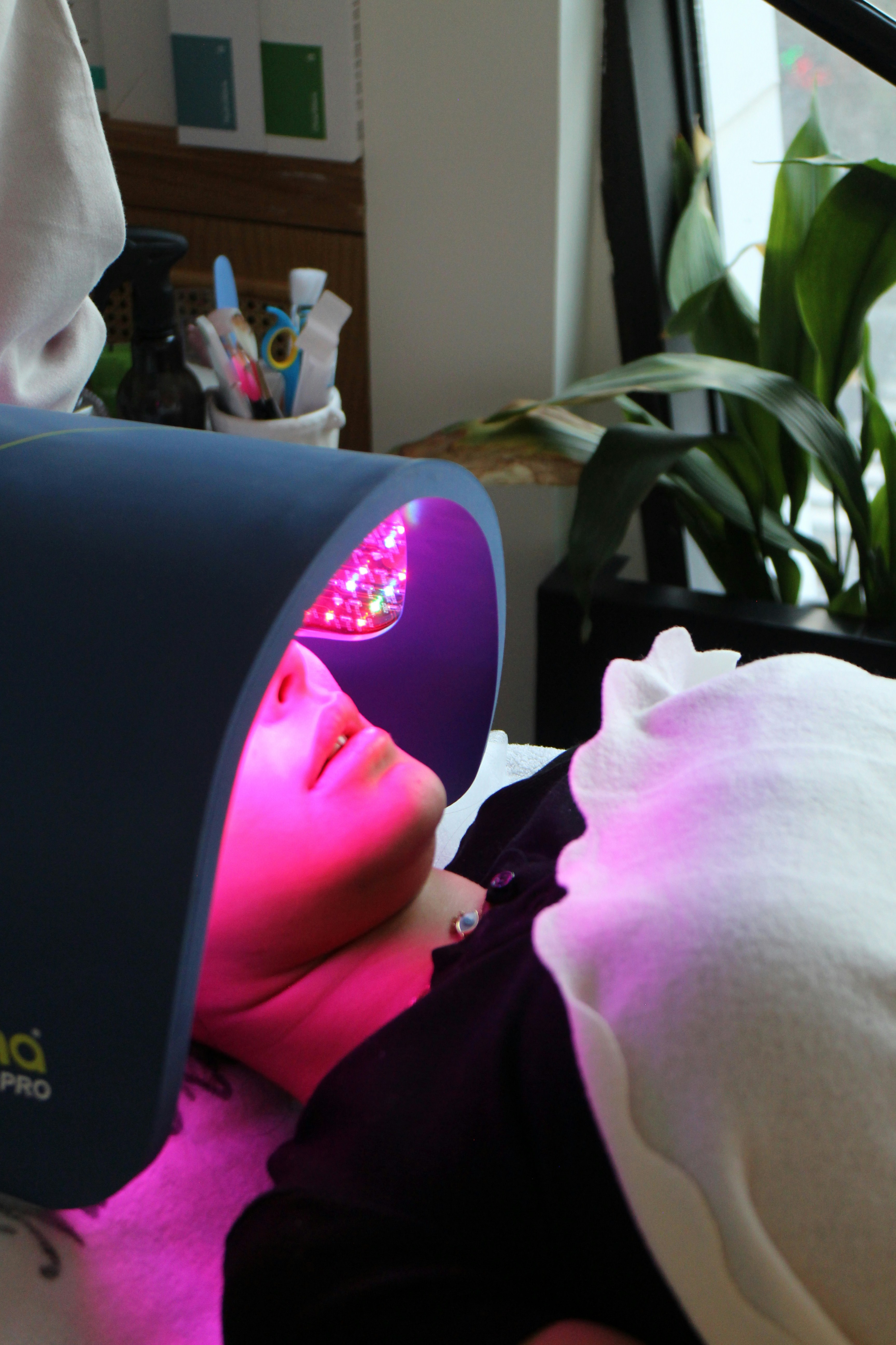 A client under an LED light therapy panel during a facial