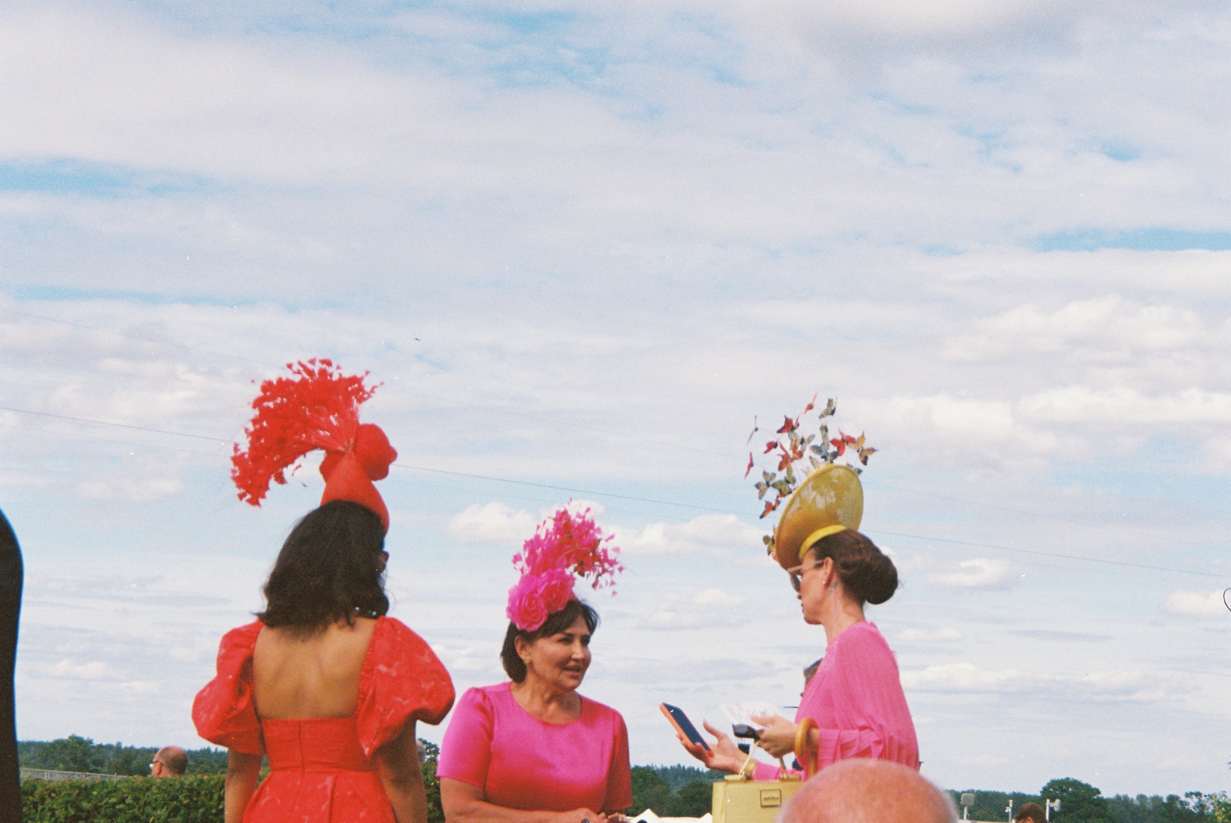 Women in vivid dresses and elaborate hats at a racecourse