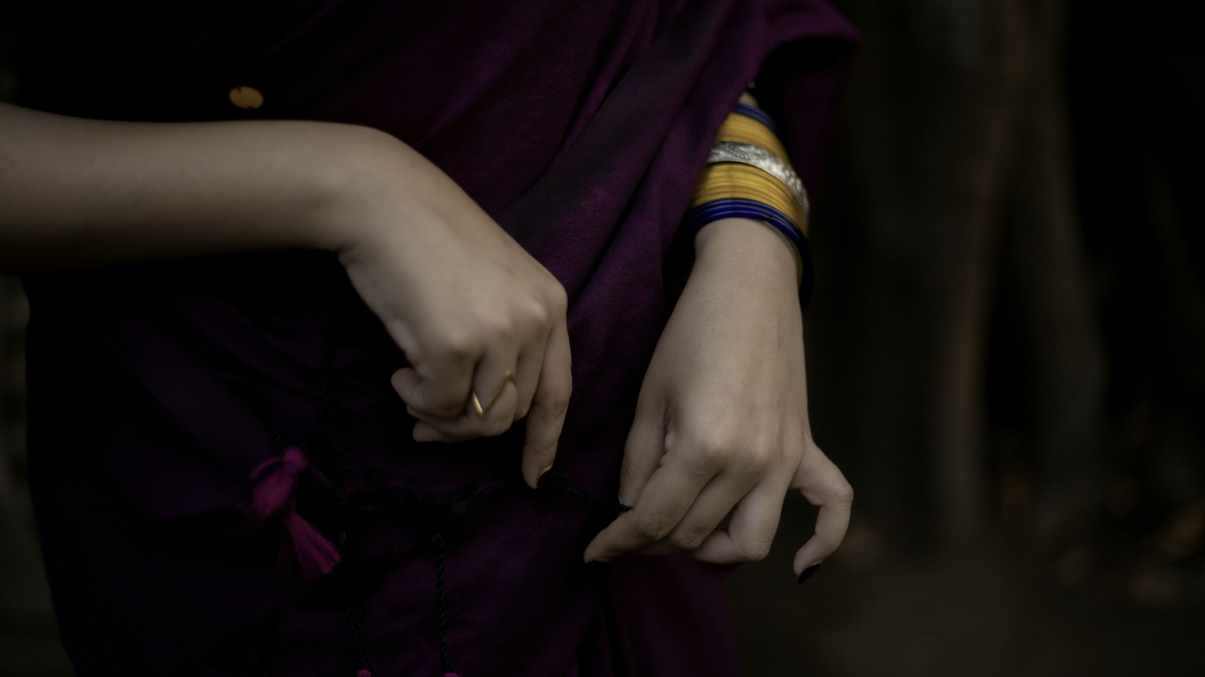 A woman's hands and bangles resting against deep plum fabric