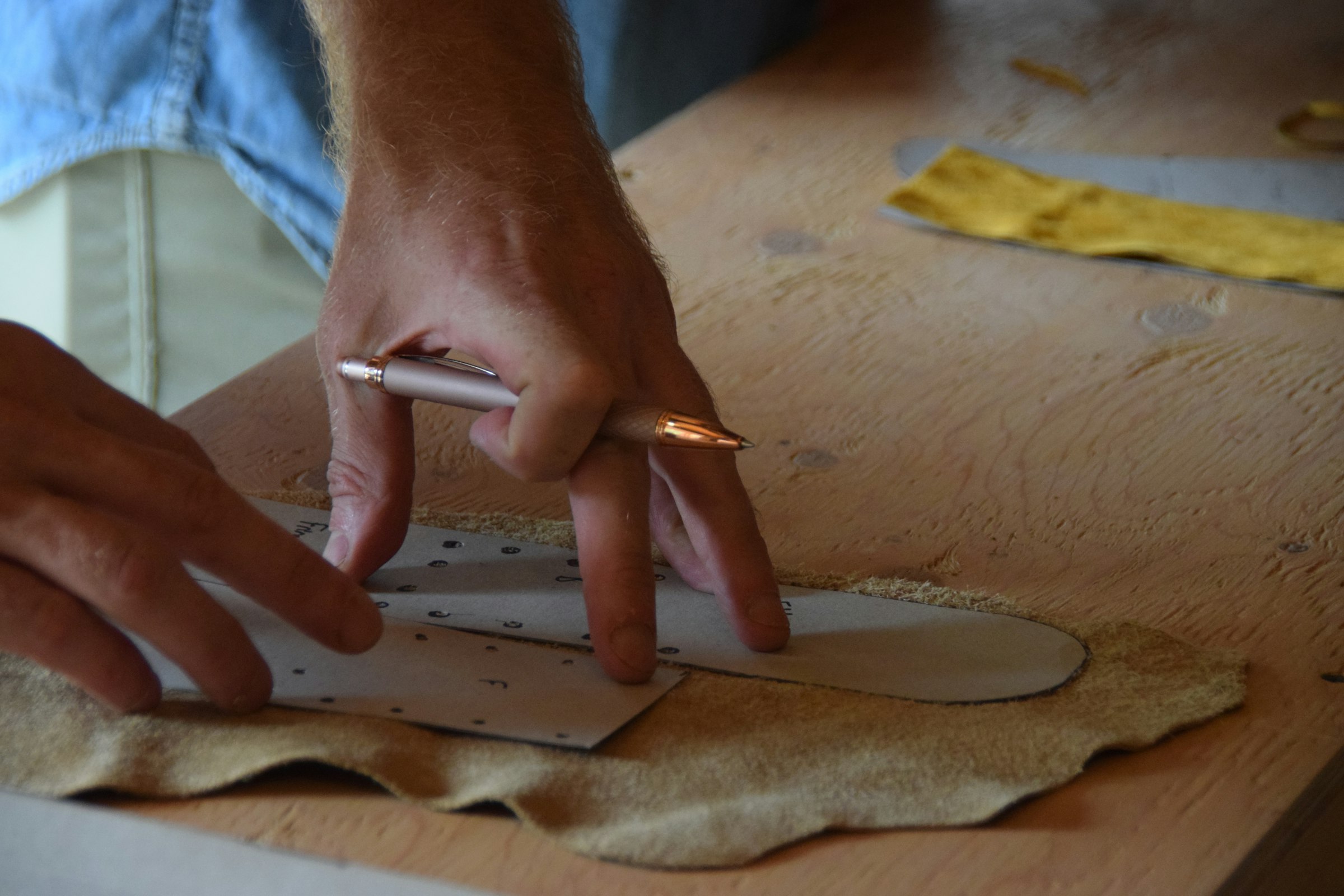 A maker tracing a pattern onto leather at a workbench