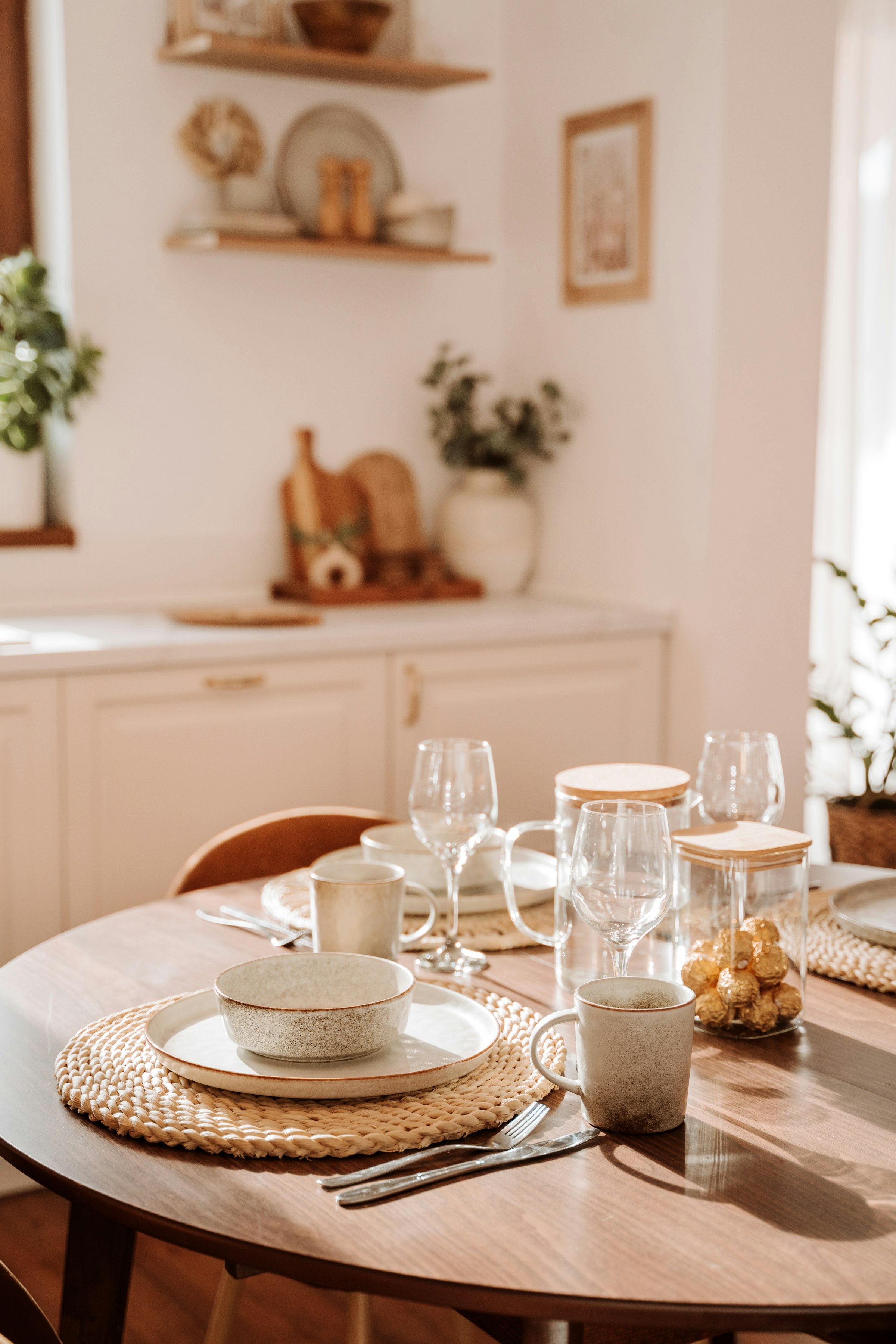 A wooden dining table laid with plates and glasses in a sunlit home