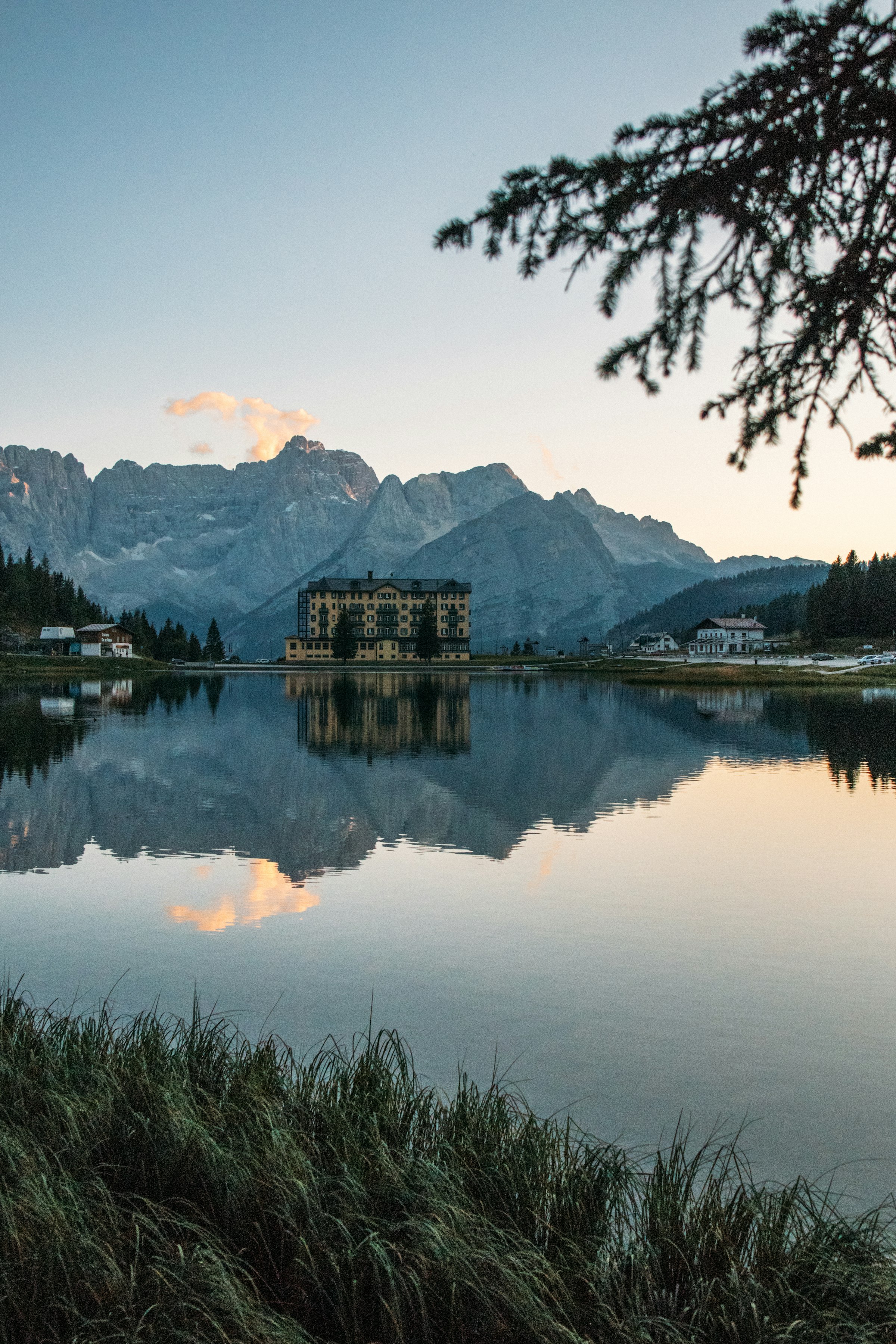 A lakeside hotel mirrored in still water at dusk beneath the Dolomites