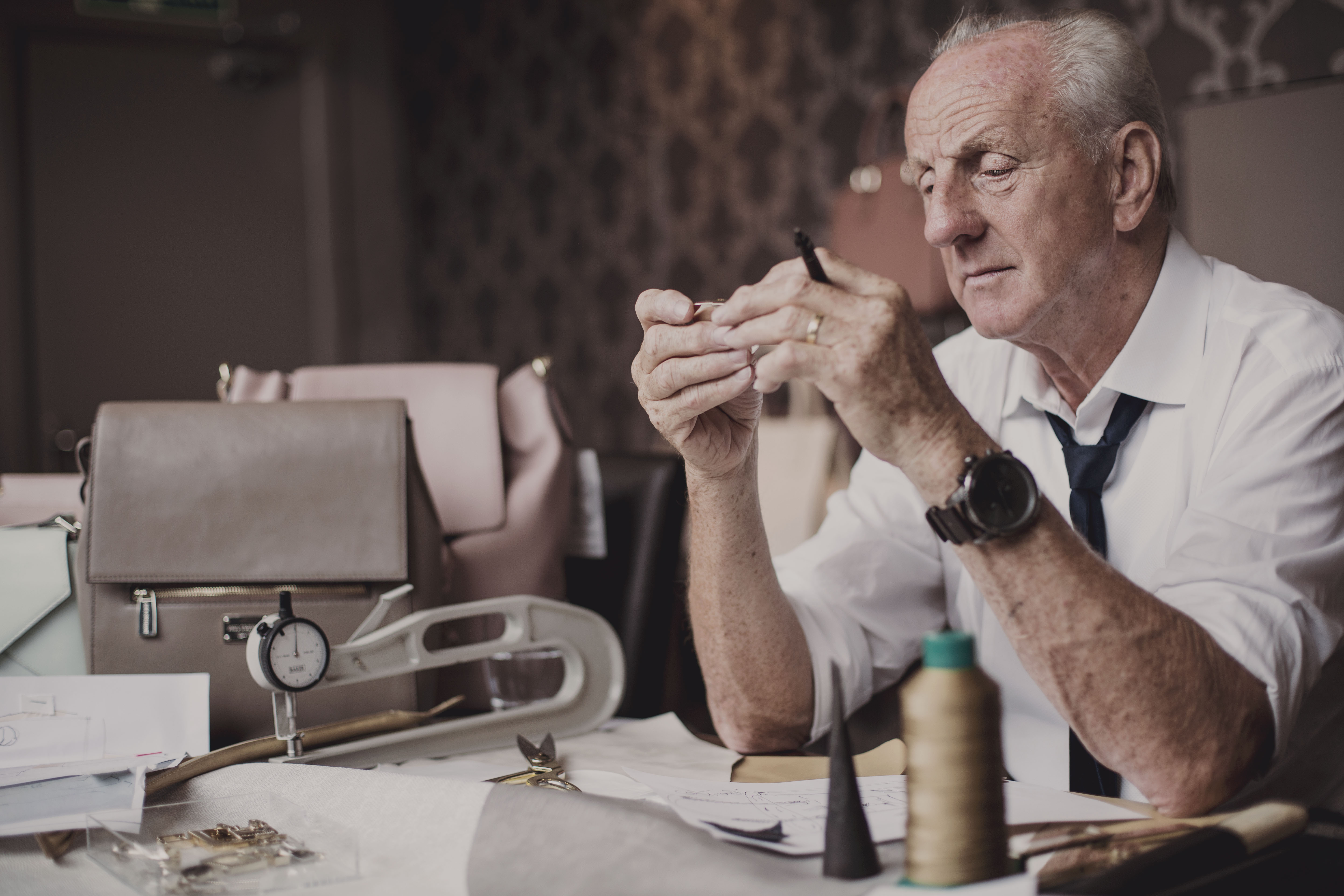 Paul Costelloe at his working desk with a handbag prototype and design drawings